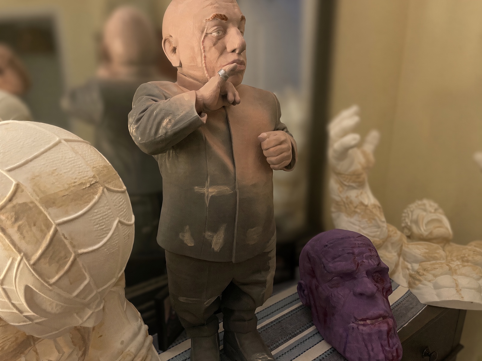 A workshop table holding a character bust, a Spider-Man head, a painted sculpted head and a printed arm, all at different stages