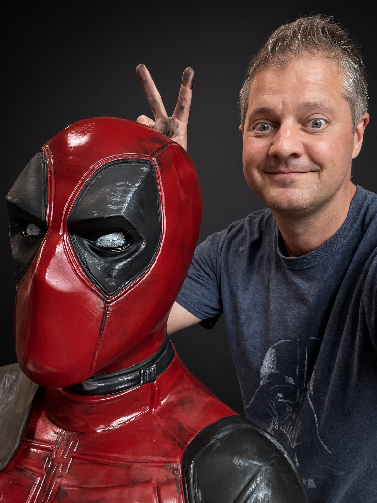 Matt Baribeau flashing a two-finger gesture behind a Deadpool bust with black detailing and weathering painted in